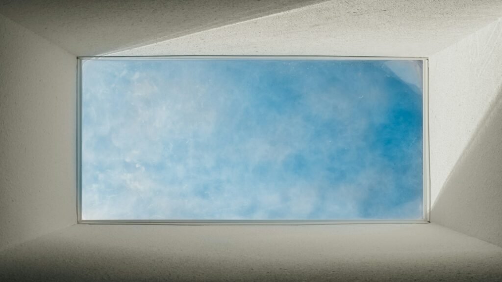 A skylight window with special tinting offers a view of a clear blue sky.