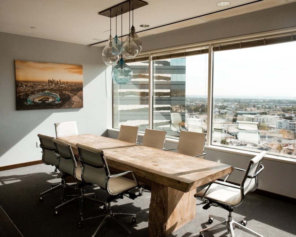 A Conference Room With A Wooden Table And Chairs, Offering A Beautiful View Of The City Through Its Window.