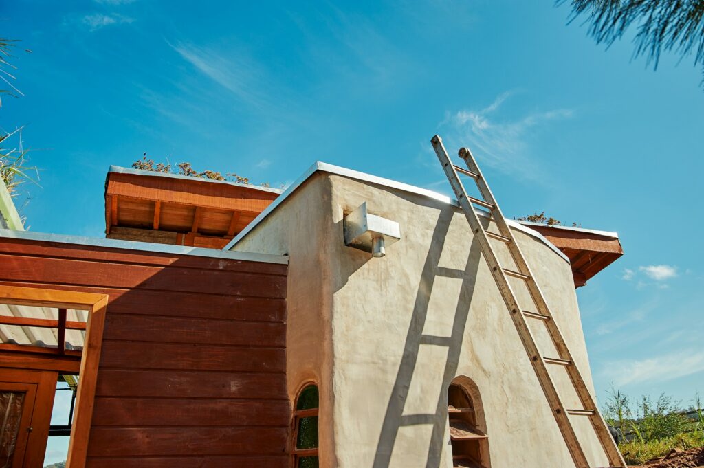 A Green Home With A Ladder On Top Of It, Showcasing Eco-Friendly Construction And Tinting.